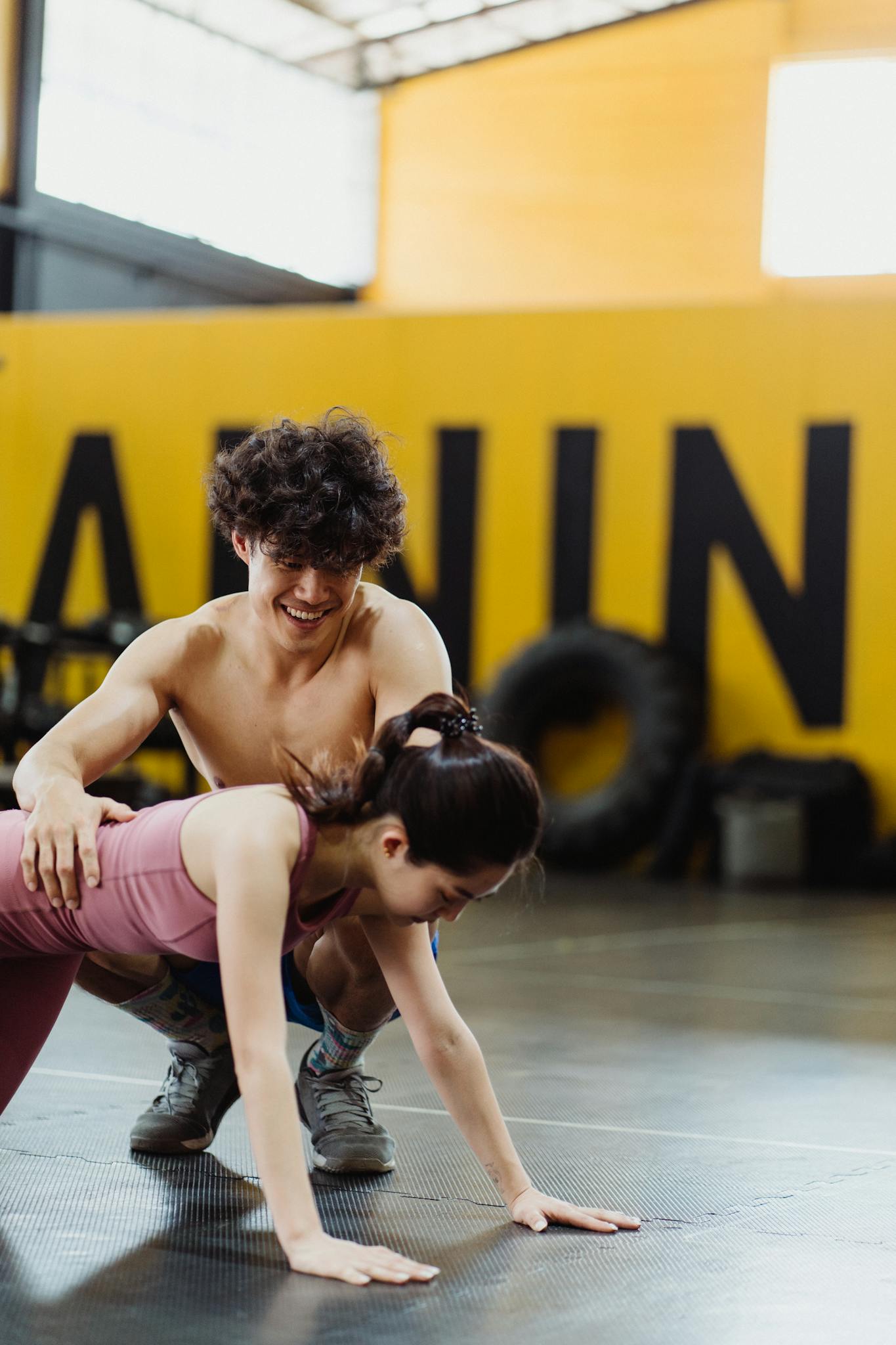 A man assists a woman during a push-up exercise in an indoor gym setting, emphasizing teamwork.